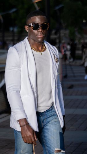 Model sports casual chic look with white blazer, cream sweater and blue jeans on runway.
