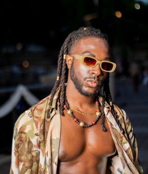 Person in camouflage jacket and orange sunglasses posing outdoors at dusk.