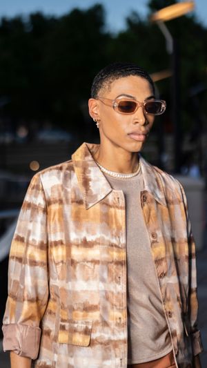 A person wearing a tie-dye patterned jacket and sunglasses poses in a series of outdoor fashion shots at dusk.