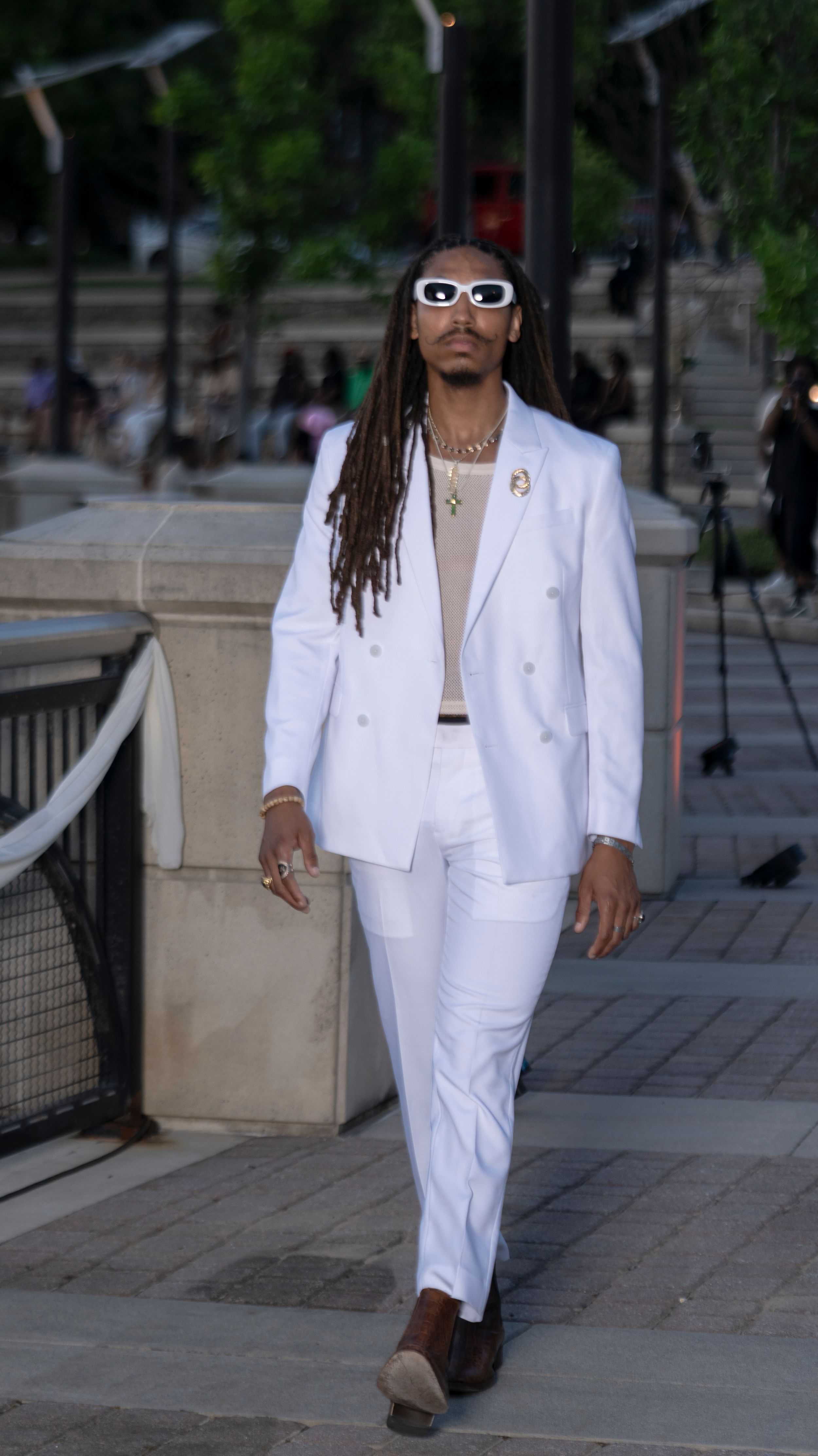 Crisp white suit with beige undershirt and statement sunglasses presented at fashion show.