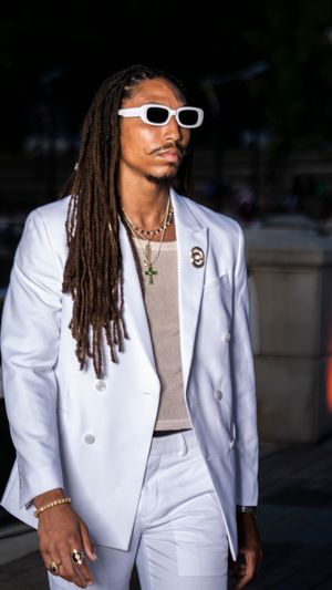 Model wearing crisp white suit and sunglasses walking outdoor runway.