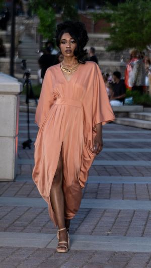 Model in flowing peach-colored dress walking on stone paved outdoor runway.
