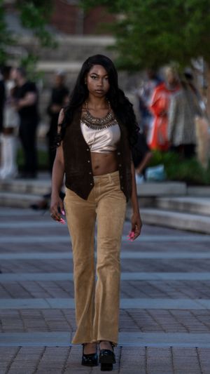 Tan corduroy pants styled with metallic top and vest for outdoor runway presentation.