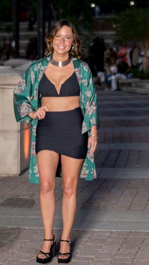 A person in a black dress and green floral kimono poses confidently on a stone paved street.