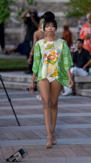 A person wearing a green and white floral outfit walks across a brick paved area in summer weather.