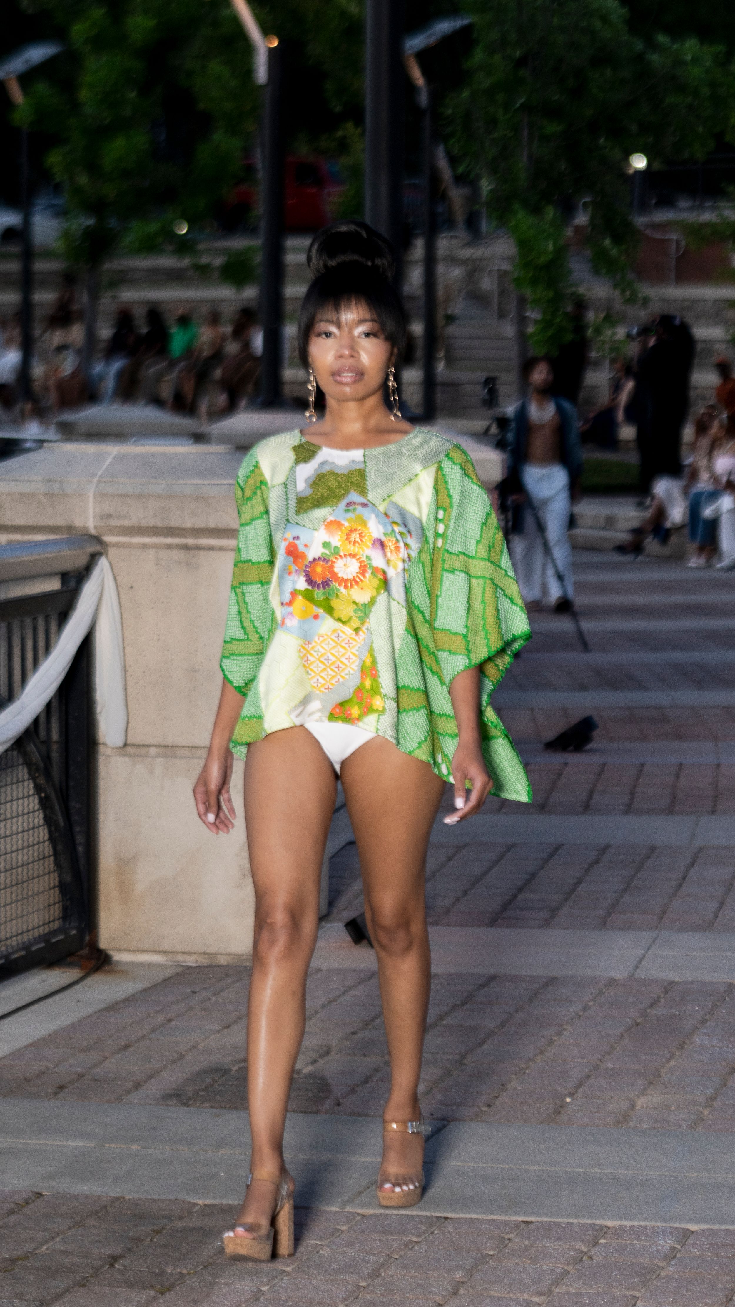Model poses in a vibrant green and floral print outfit on an outdoor stone walkway.