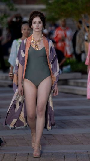 Model showcases grey swimsuit and floral kimono with statement necklace on outdoor catwalk.