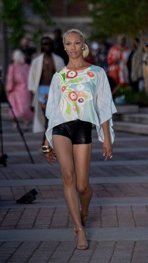Dancer in floral crop top and black shorts performs dynamic movement sequence on brick paved outdoor area.