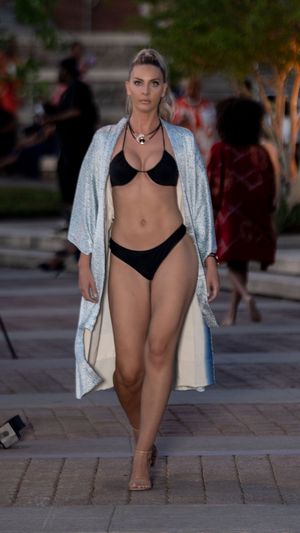 Model presents black bikini with shimmering silver cover-up during outdoor fashion show.
