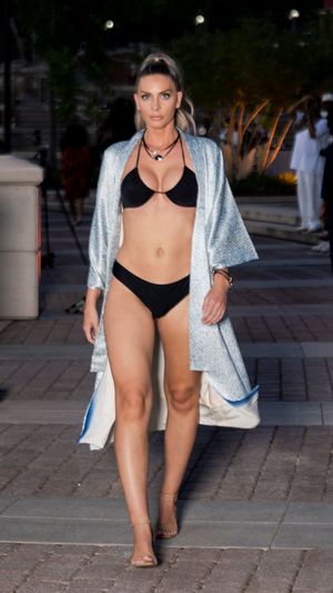 Model showcases sparkly silver cover-up with black swimwear at outdoor fashion event.