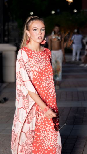 Person wearing a flowing red and white patterned dress poses dramatically on stone steps.