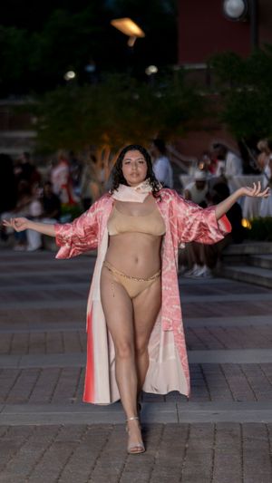 Model in pink robe and beige undergarments poses confidently on outdoor brick patio during fashion shoot.