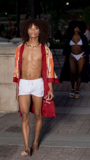 A person in white shorts and a red patterned top poses on outdoor steps in a fashion photoshoot series.