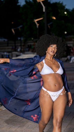 Model in white lingerie poses dramatically with flowing navy blue fabric against outdoor backdrop.