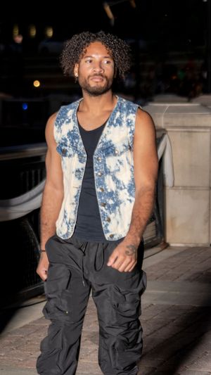 Person wearing tie-dye denim vest and black cargo pants poses confidently at night.