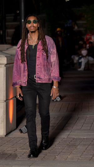 Model wearing pink denim jacket and black pants poses on outdoor runway.