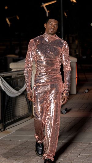 Person walks runway in full-length shimmering rose gold sequined jumpsuit at fashion show.