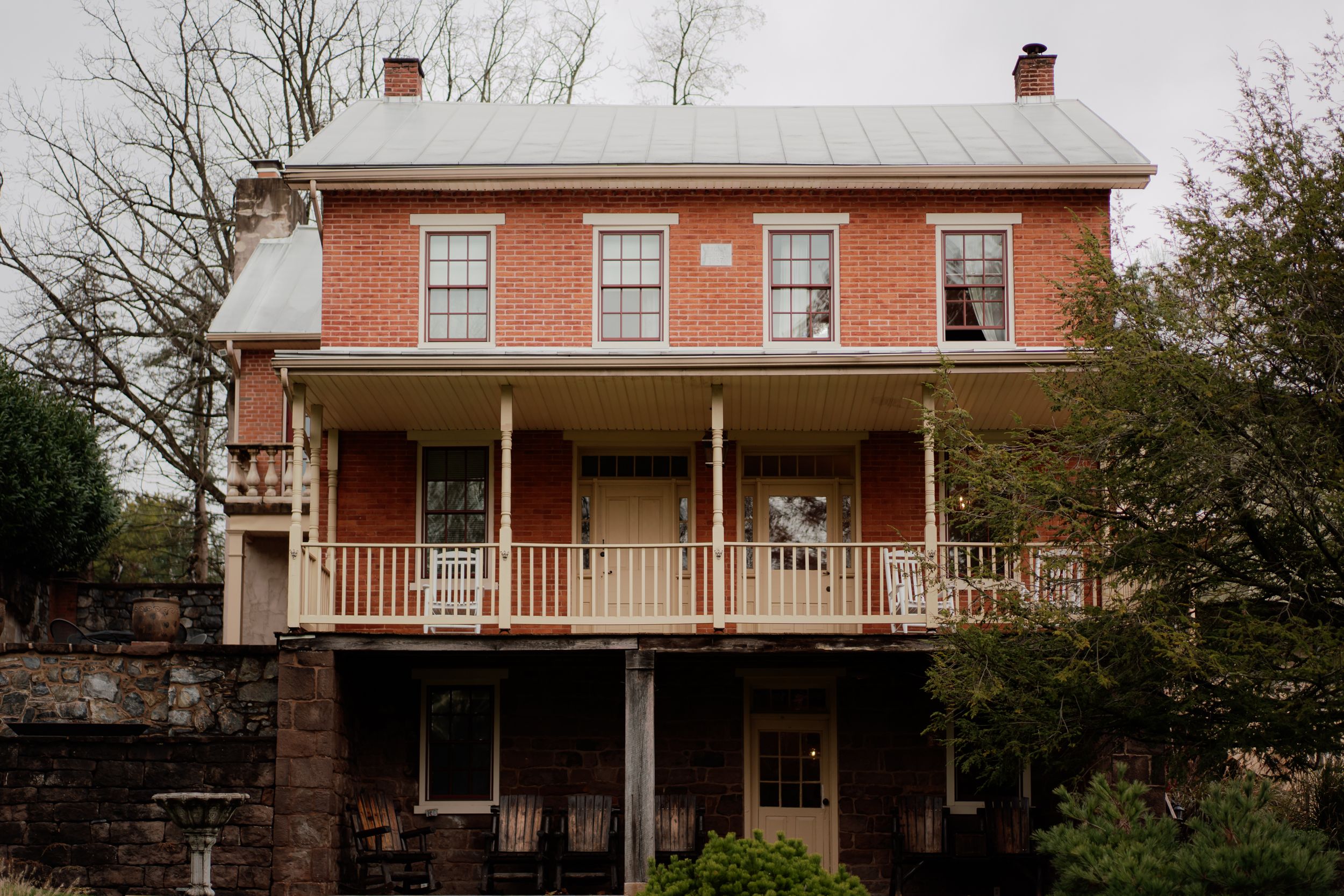 Exterior view of a classic red brick mansion with white trim and multiple windows on a cloudy day.