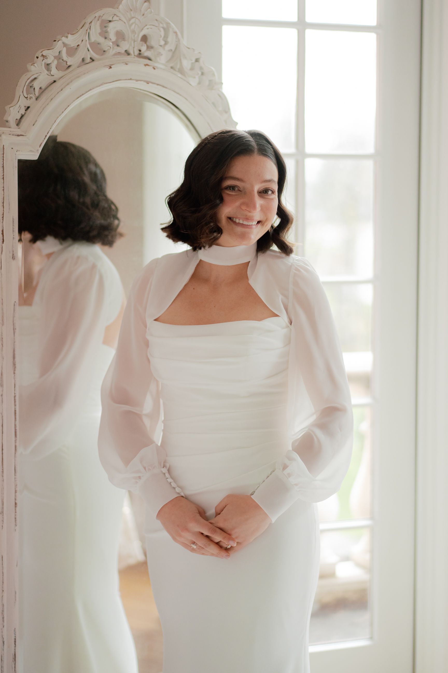 Elegant white wedding dress with puff sleeves shown in bright sunlit room.