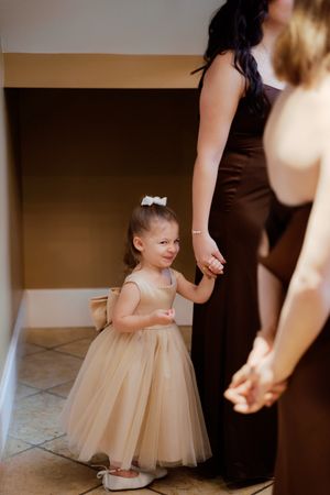 Young flower girl in a cream tulle dress standing near adults at a wedding.