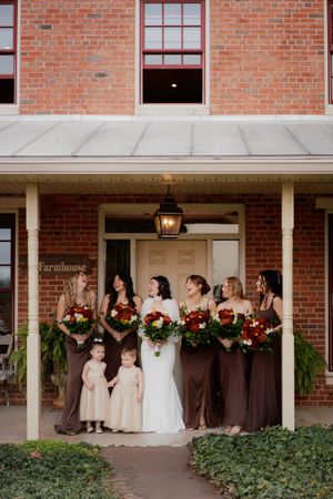 Wedding party posing on brick building porch decorated with festive red and green holiday garland.