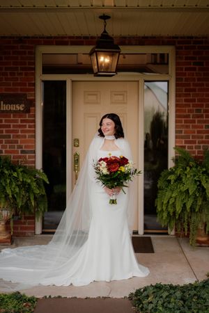 Bride in flowing white gown standing on brick porch with hanging ferns.