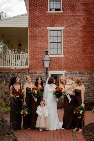 Bridal party in alternating brown and white dresses poses outside a brick building.