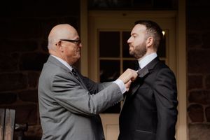 Groomsmen adjusting ties and helping each other prepare in formal attire.