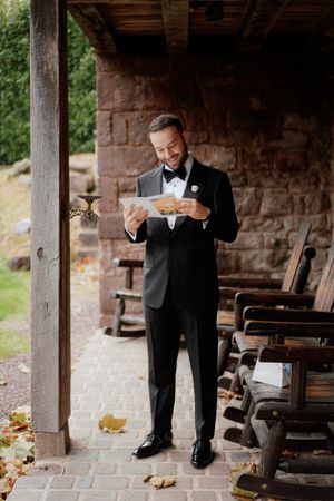 Groom reading emotional letter under rustic stone archway.