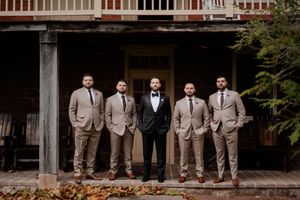 Wedding party in coordinated attire posing on a rustic porch with wooden railings.