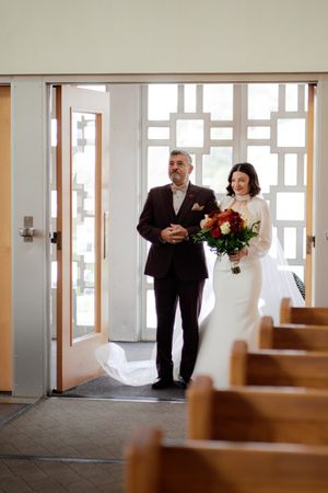 Church interior with wooden pews and natural light streaming through windows during wedding ceremony.
