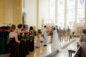 Church interior with stained glass windows and rows of dark wooden pews during a ceremony.