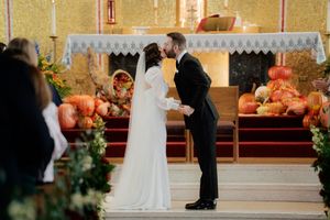 Wedding ceremony in progress inside a church with golden decor and pumpkin arrangements.