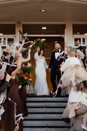 Wedding party celebrates on stone steps with white streamers and confetti in evening light.
