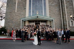 Panoramic view of wedding guests gathered outside a grand stone church building.
