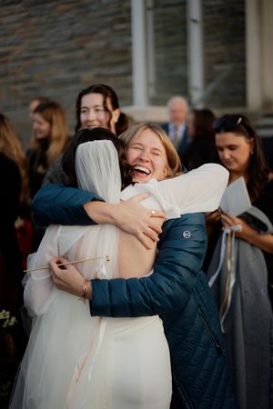 Joyful embraces shared between wedding guests outside a stone church building.