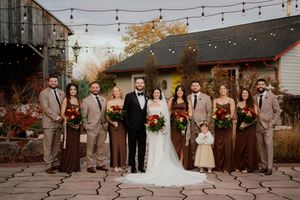 Wedding party poses under string lights at dusk with autumn colors in the background.