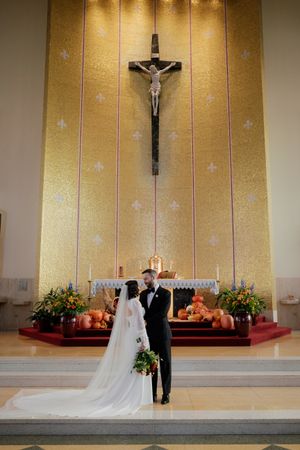 Wedding ceremony at altar with golden backdrop and crucifix in a Catholic church setting.