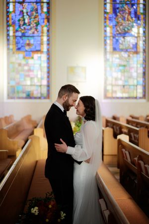 A romantic wedding moment captured in a church with beautiful stained glass windows illuminating the scene.
