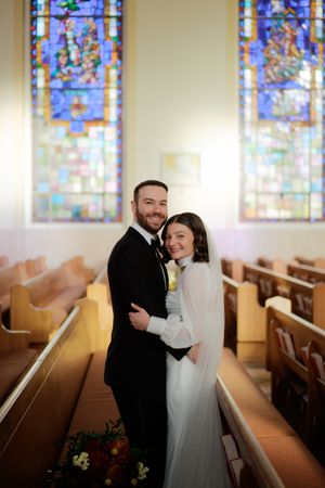 A couple shares an intimate moment in a church with stained glass windows and wooden pews.