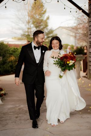Newlyweds walk and laugh together under string lights on their wedding day.