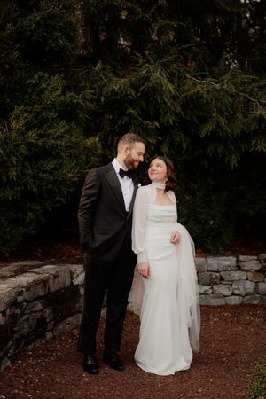 A romantic wedding couple embraces against a natural stone wall backdrop during golden hour.
