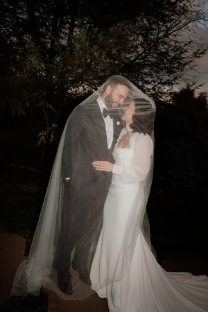 Romantic evening wedding portrait with flowing veil against dark background.