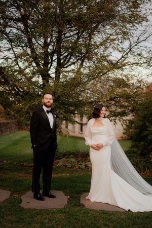Wedding couple poses in a park with autumn trees and long flowing veil creating dramatic composition.