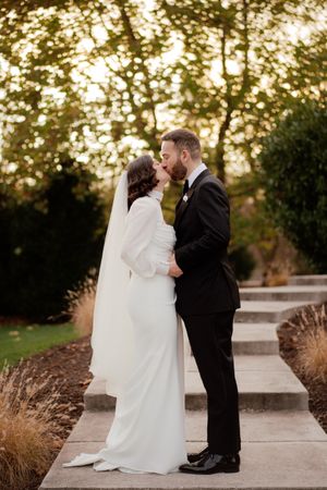A romantic wedding couple shares an intimate moment at sunset on a stone path surrounded by autumn grasses.