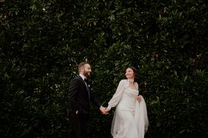 A couple shares romantic moments against a backdrop of green hedges.