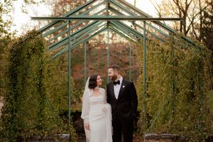 Wedding couple posing in front of a greenhouse with autumn foliage.