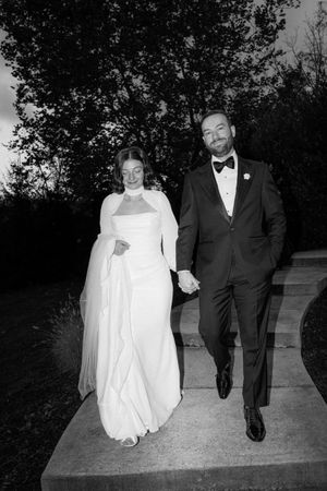 Couple walking along pathway at dusk in formal wedding attire.