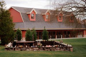 A rustic red barn wedding venue with wooden benches set up for an outdoor ceremony in a pastoral setting.