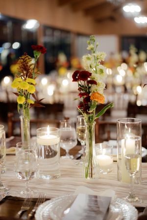 Wedding reception table settings with delicate bud vases, candles and glassware.